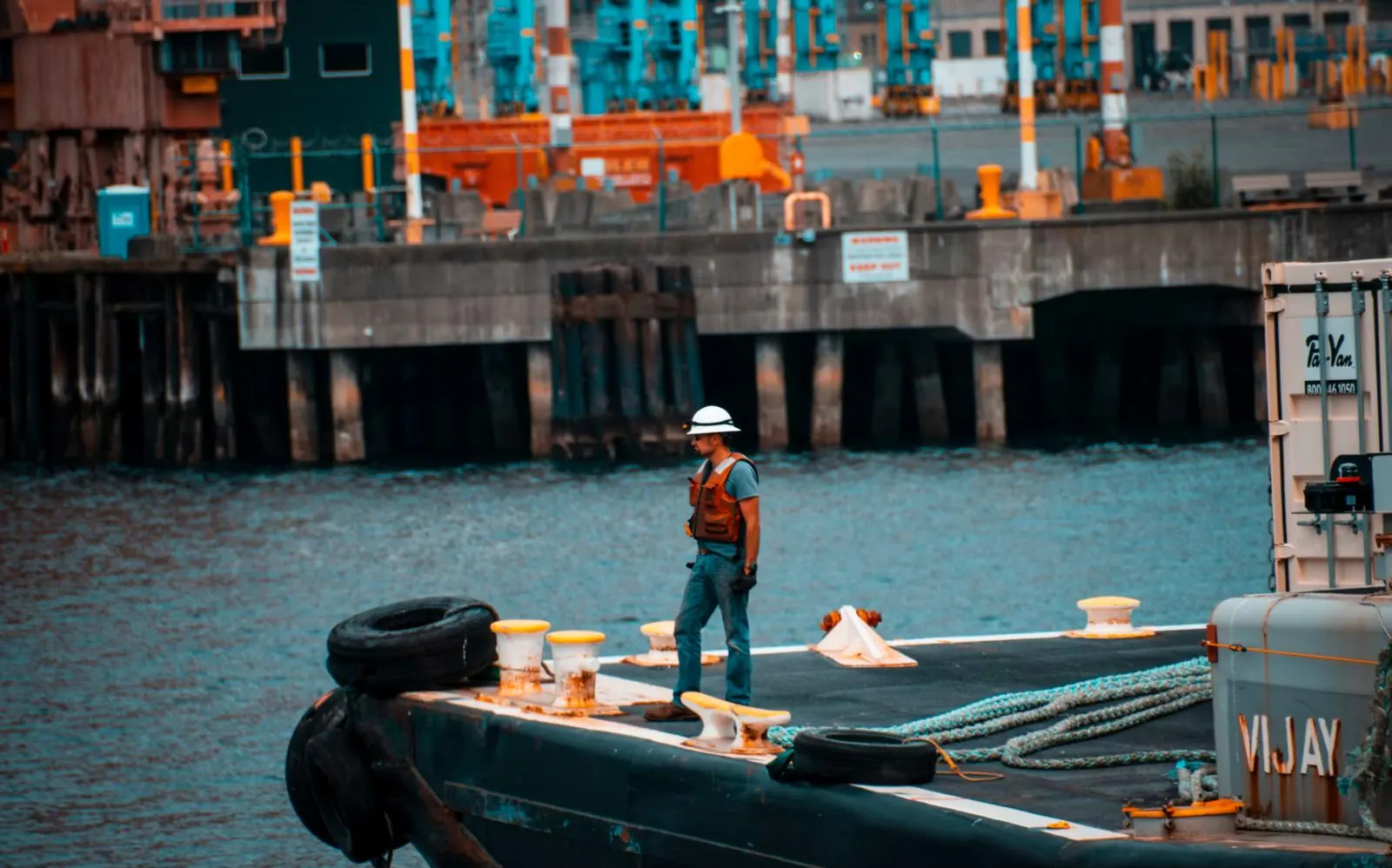 A worker standing at the edge of a quay beside a moored vessel